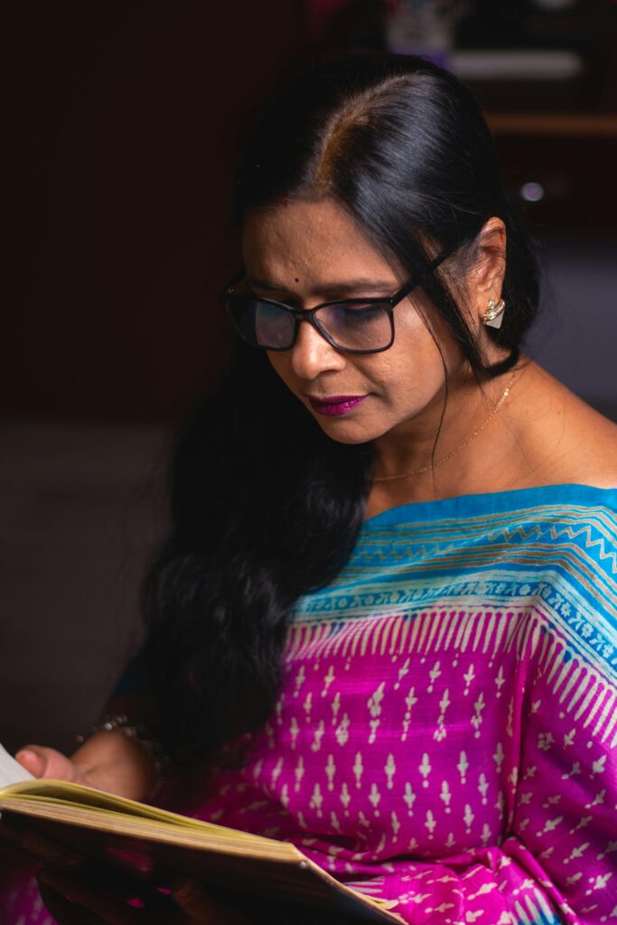 Portrait of a woman in a sari reading indoors, showcasing cultural attire and calm focus.